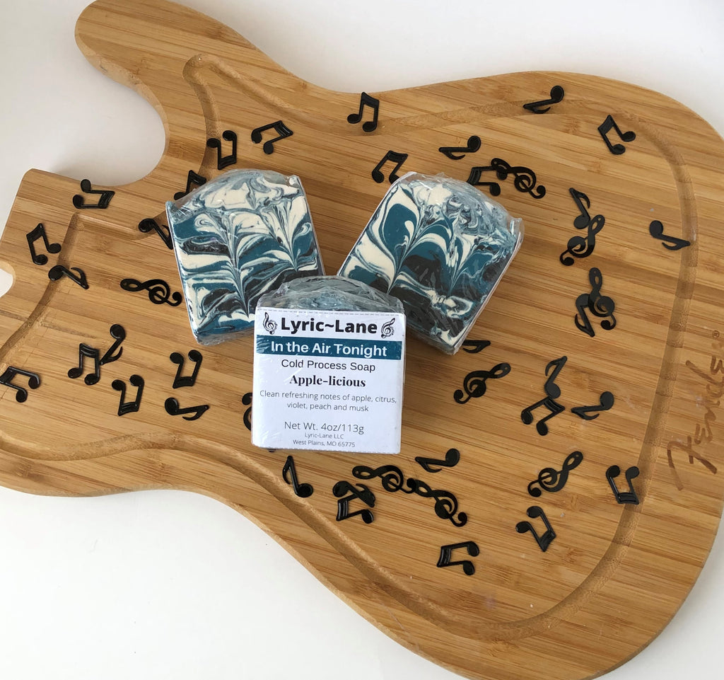 Three 4oz bars of In the Air Tonight cold processed soap on a wood guitar shape with scattered music notes. Scented with notes of apple, citrus, violet, peach and musk. Designed with a teal, black and white swirl pattern. Made by Lyric-Lane