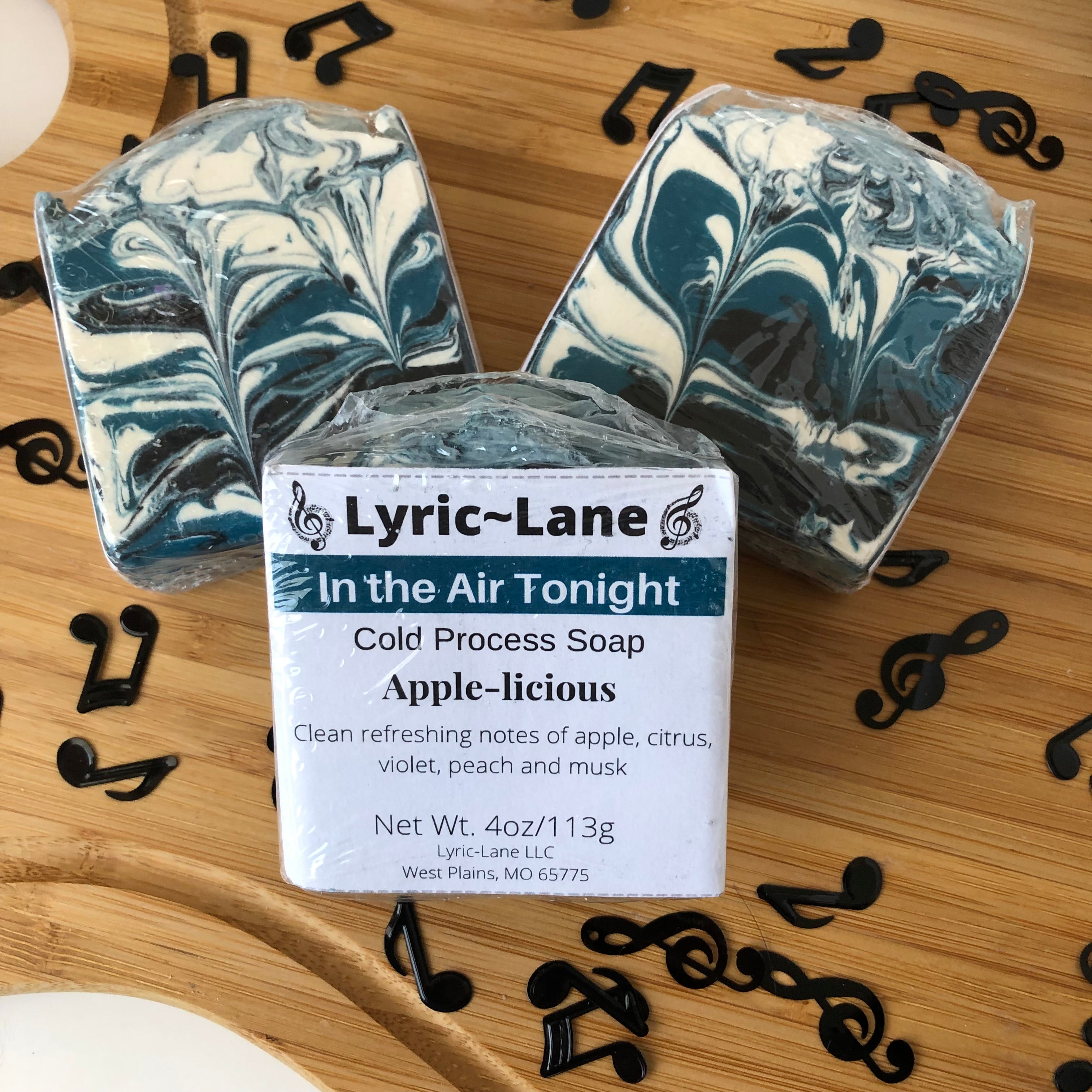 Three 4oz bars of In the Air Tonight cold processed soap on a wood guitar shape with scattered music notes. Scented with notes of apple, citrus, violet, peach and musk. Designed with a teal, black and white swirl pattern. Made by Lyric-Lane