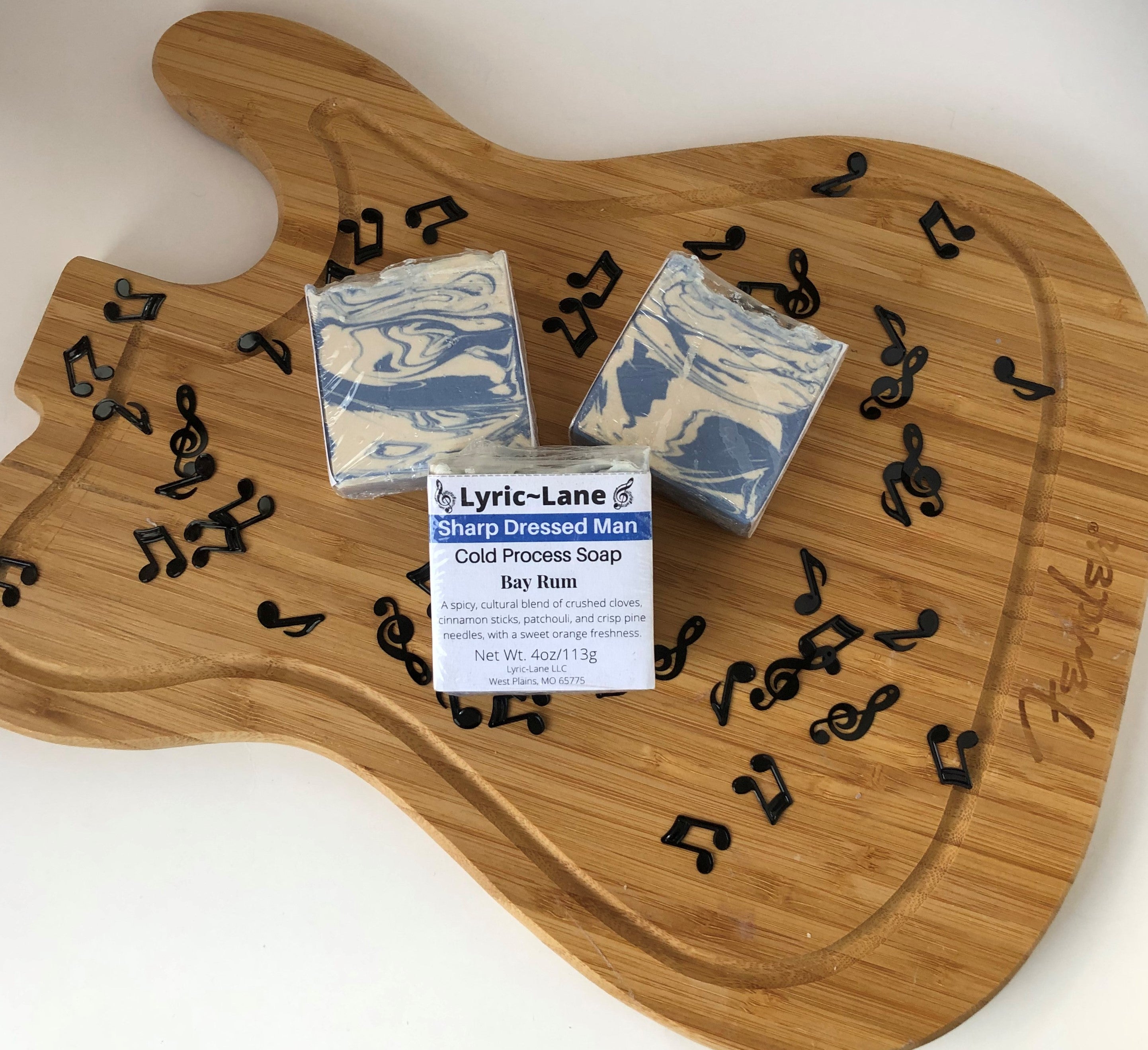 Three 4oz bars of Sharp Dressed Man cold processed soap on a wood guitar shape with scattered music notes. Scented with a bay rum blend. Designed with a blue and white swirl pattern. Made by Lyric-Lane