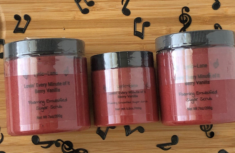 Three jars of crimson Lovin' Every Minute of It-Berry Vanilla scented whipped emulsified sugar scrub. Two 7 oz PET plastic jars and one 3.5 oz jar in the middle on a wood background with scattered music notes. Made by Lyric-Lane.